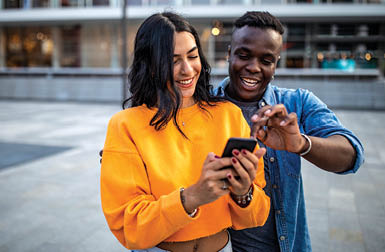 Beautiful, cheerful couple looking at smart phone, choosing the best photo for social media