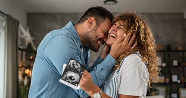 The photo shows a young couple looking at an ultrasound scan together, their expressions filled with joy and excitement because they are expecting a baby